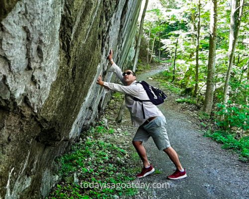 Hike in Central Switzerland, on a forest road, man pretending to hold the rockface