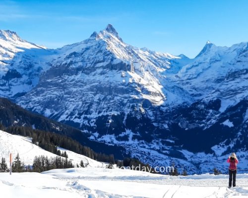 Winter hiking in Grindelwald, Sophia taking a photo with Grindelwald in and Alpes in the background