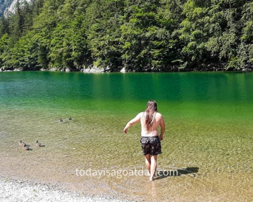 One of the best things to do in Appenzell, man witth long hair wading into the clear Seealpsee water